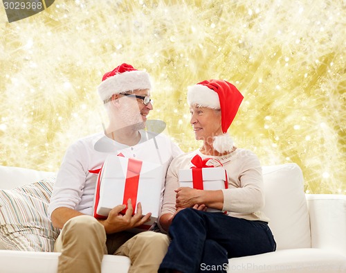 Image of happy senior couple in santa hats with gift boxes