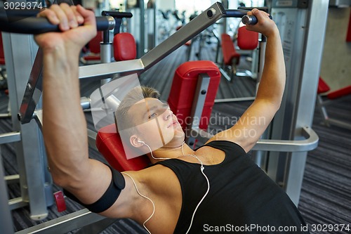 Image of young man with earphones exercising on gym machine