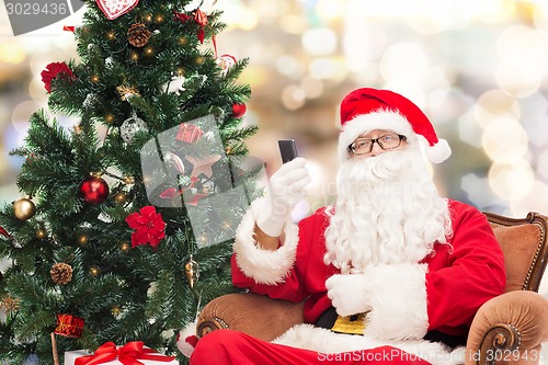 Image of santa claus with smartphone and christmas tree