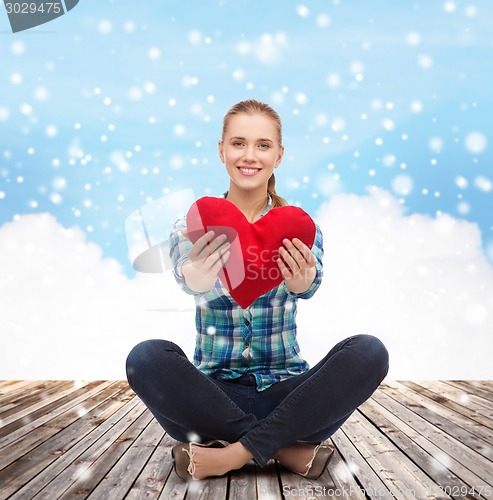 Image of young woman with red heart pillow sitting on floor