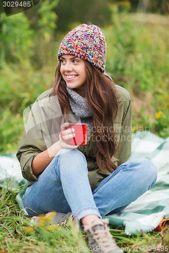 Image of smiling young woman with cup sitting in camping