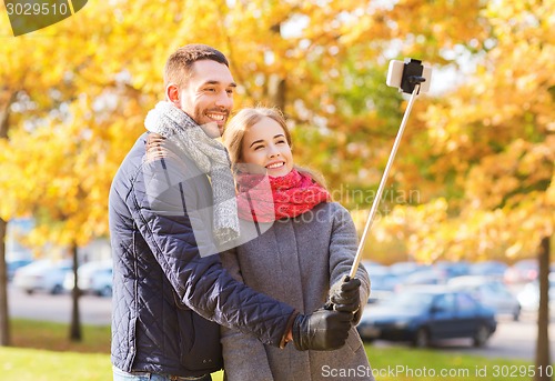 Image of smiling couple with smartphone in autumn park