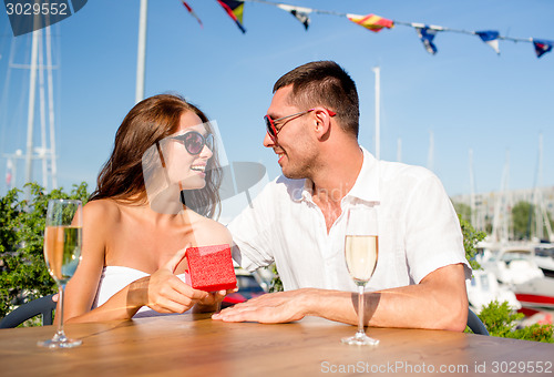 Image of smiling couple with champagne and gift at cafe