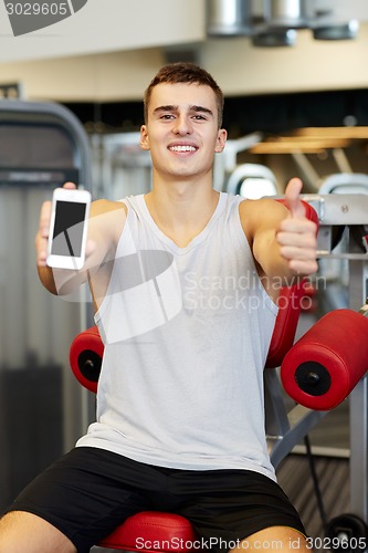 Image of smiling young man with smartphone in gym