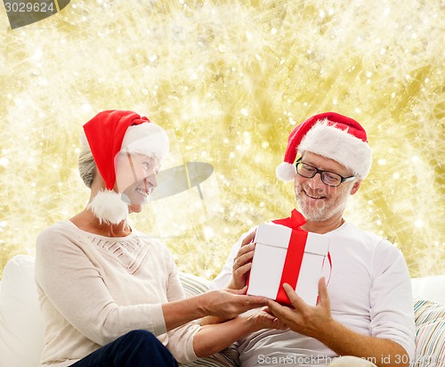 Image of happy senior couple in santa hats with gift box