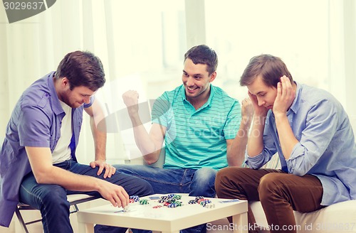 Image of happy three male friends playing poker at home