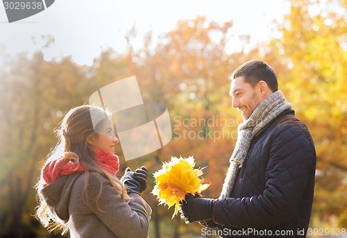 Image of smiling couple with bunch of leaves in autumn park