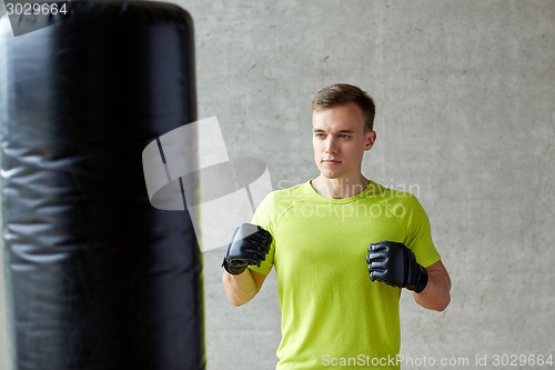 Image of young man in gloves boxing with punching bag