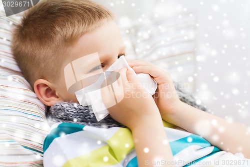 Image of ill boy blowing nose with tissue at home