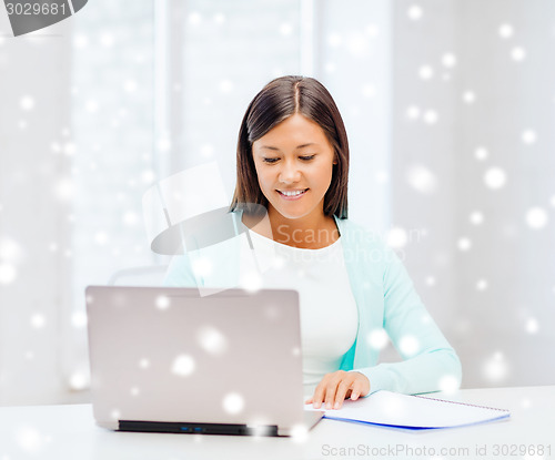 Image of smiling young woman with laptop and notebook
