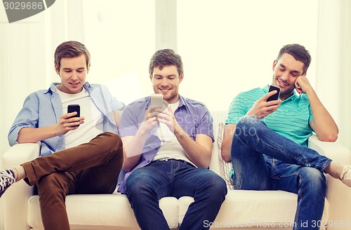 Image of smiling friends with smartphones at home