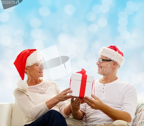 Image of happy senior couple in santa hats with gift box