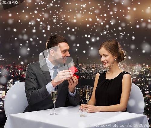 Image of smiling couple with red gift box at restaurant
