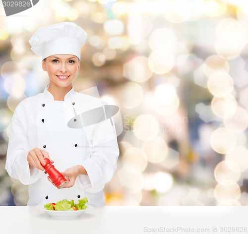 Image of smiling female chef spicing vegetable salad
