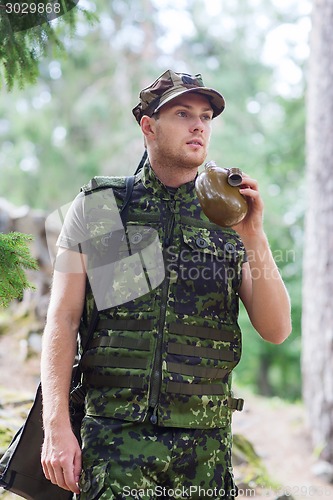 Image of young soldier with gun and flask in forest