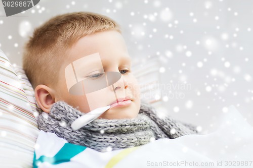 Image of ill boy with thermometer lying in bed at home