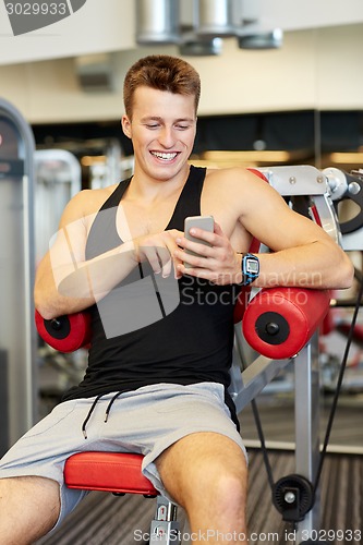 Image of smiling young man with smartphone in gym