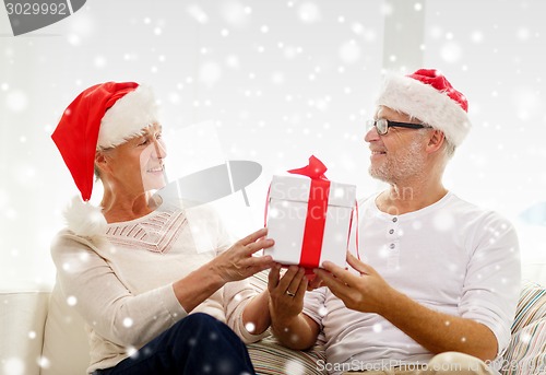 Image of happy senior couple in santa hats with gift box
