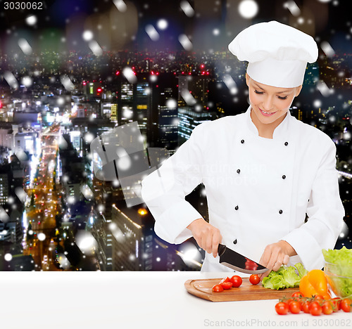 Image of smiling female chef chopping vegetables