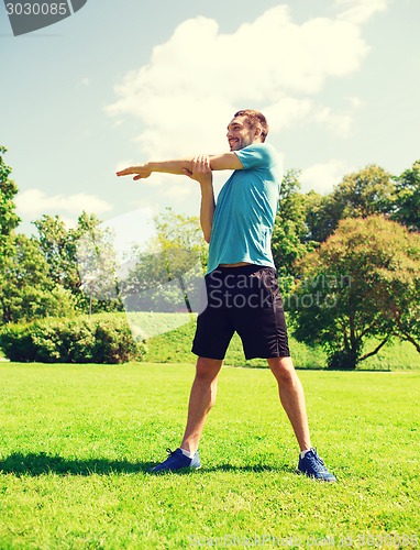 Image of smiling man stretching outdoors