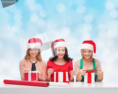 Image of smiling women in santa helper hats packing gifts