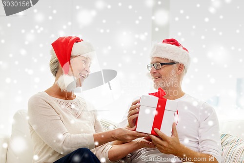 Image of happy senior couple in santa hats with gift box