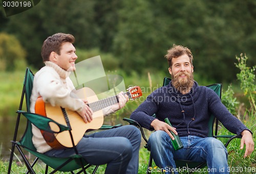 Image of smiling tourists playing guitar in camping