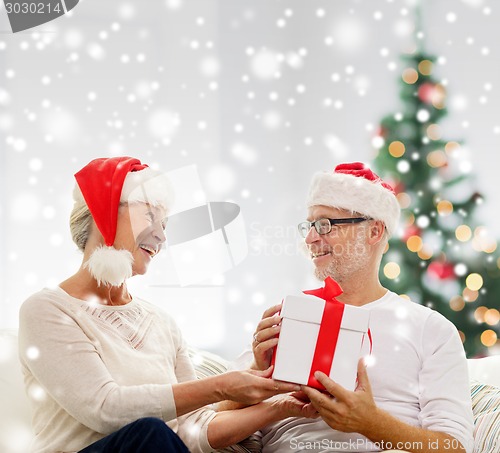 Image of happy senior couple in santa hats with gift box