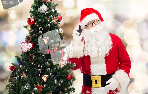 Image of santa claus with smartphone and christmas tree