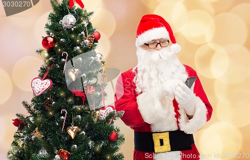 Image of santa claus with smartphone and christmas tree