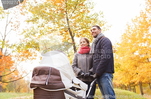 Image of smiling couple with baby pram in autumn park