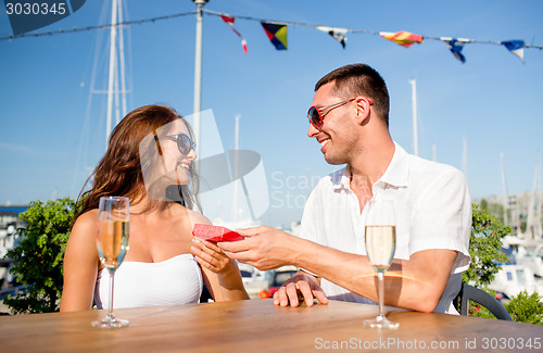 Image of smiling couple with champagne and gift at cafe