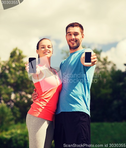 Image of two smiling people with smartphones outdoors