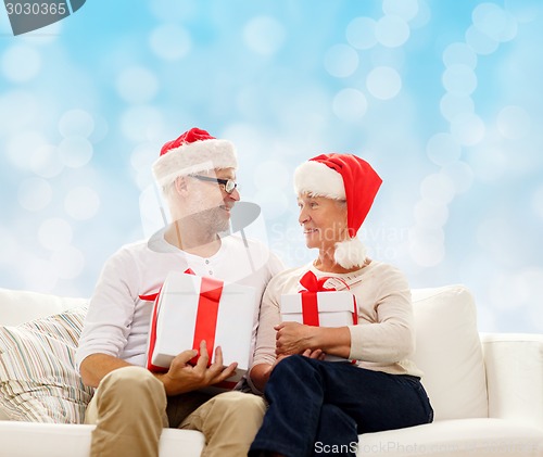 Image of happy senior couple in santa hats with gift boxes