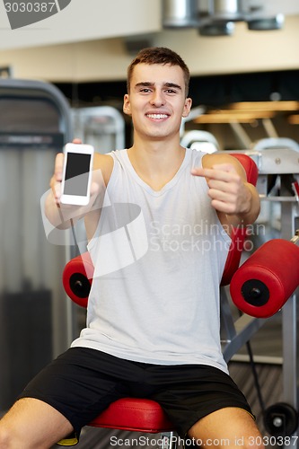 Image of smiling young man with smartphone in gym
