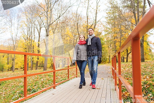 Image of smiling couple hugging on bridge in autumn park