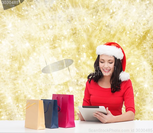 Image of smiling woman in santa hat with bags and tablet pc