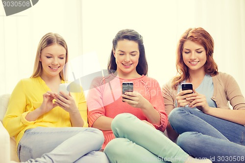 Image of smiling teenage girls with smartphones at home