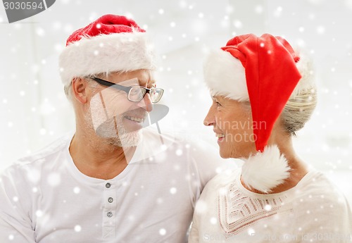 Image of happy senior couple in santa helper hats at home