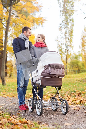 Image of smiling couple with baby pram in autumn park