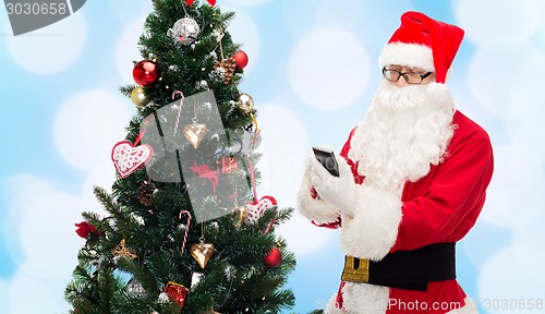 Image of santa claus with smartphone and christmas tree