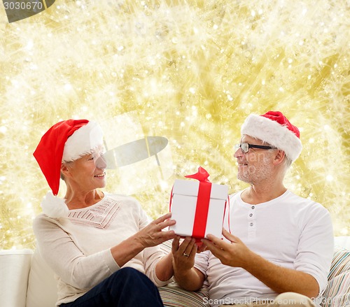 Image of happy senior couple in santa hats with gift box