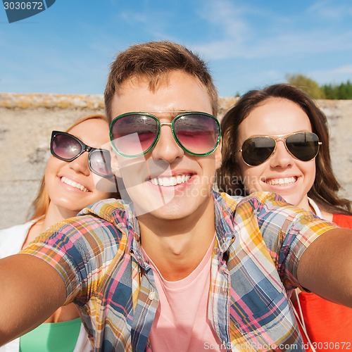 Image of group of smiling friends taking selfie outdoors