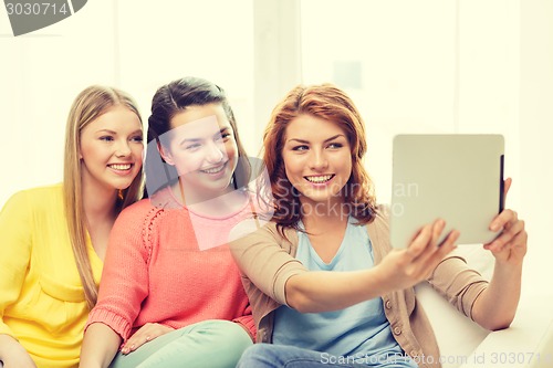 Image of three smiling teenage girls with tablet pc at home