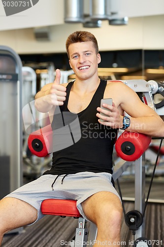 Image of smiling young man with smartphone in gym