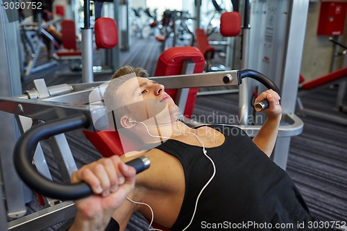 Image of young man with earphones exercising on gym machine