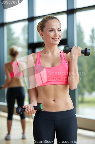 Image of young sporty woman with dumbbells flexing biceps