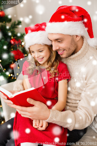 Image of smiling father and girl in santa hats reading book