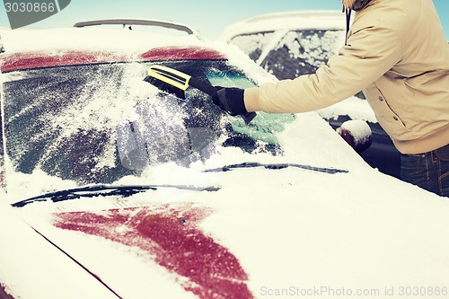 Image of man cleaning snow from car windshield with brush