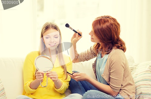 Image of two smiling teenage girls applying make up at home